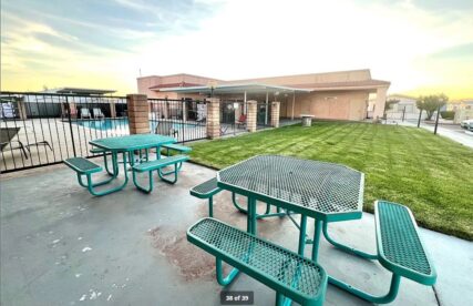 Green tables, a grassy area and the pool in a gated background.
