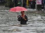 Woman walking through flood water holding a pink umbrella.