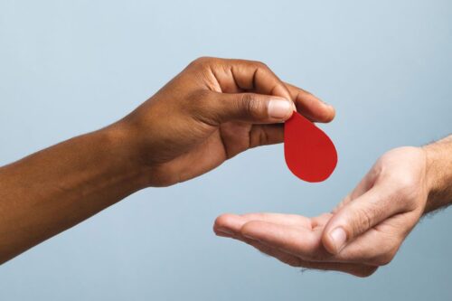 Black person hand giving a paper blood drop to a white person hand for the concept of giving blood.